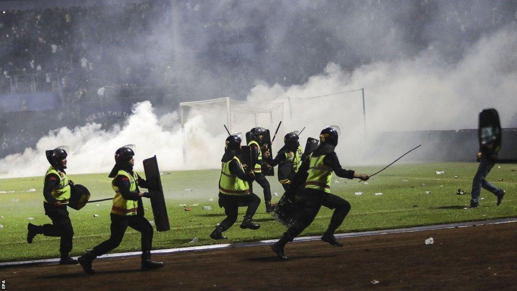 Police officers runs as they try to stop soccer fans from entering the pitch during a clash between fans at Kanjuruhan Stadium