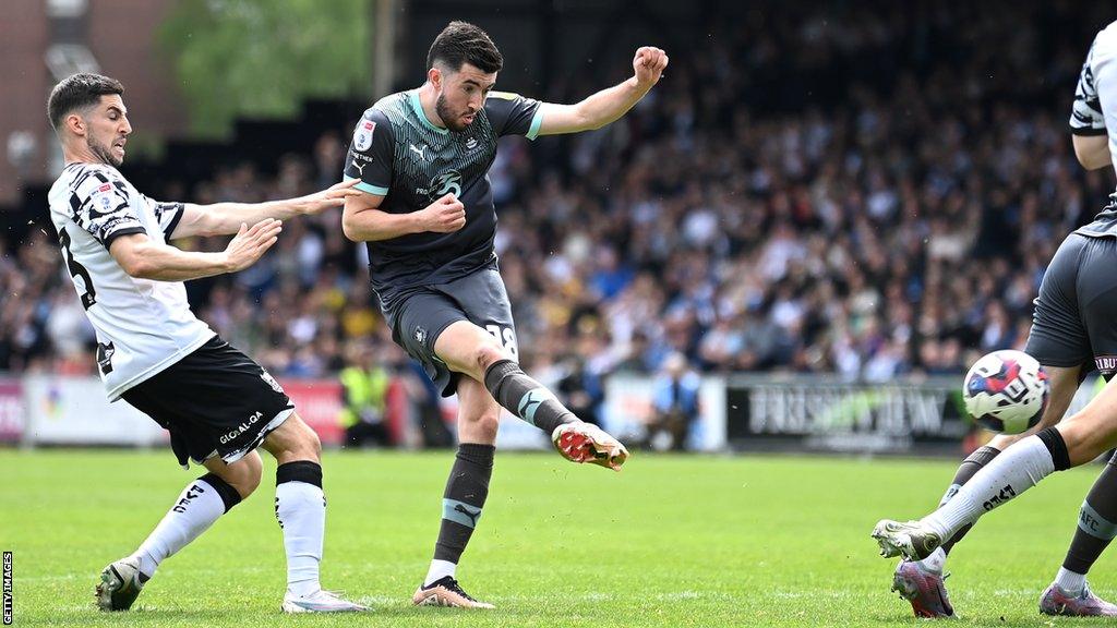 Finn Azaz of Plymouth Argyle scores the team's third goal whilst under pressure from Tom Pett of Port Vale