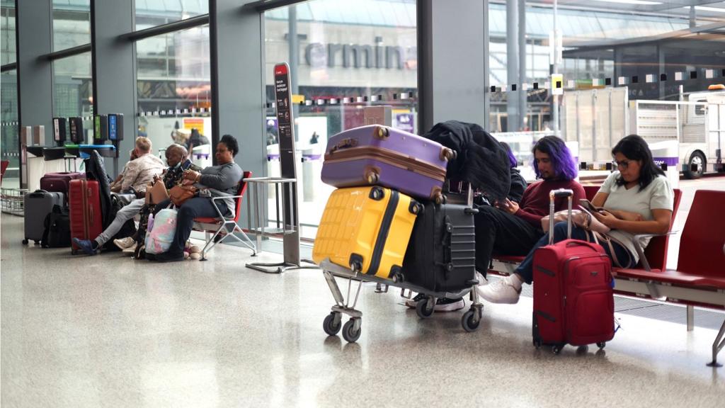 Passengers sit with their luggage in chairs at Heathrow Airport