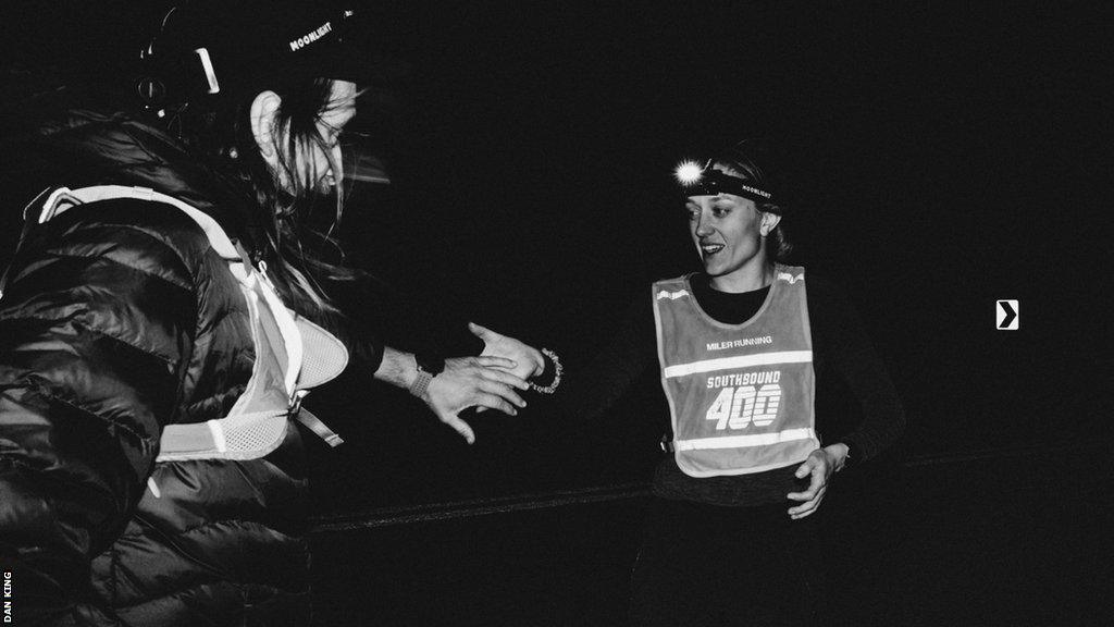 Two runners pass running duties in the dark while wearing headtorches