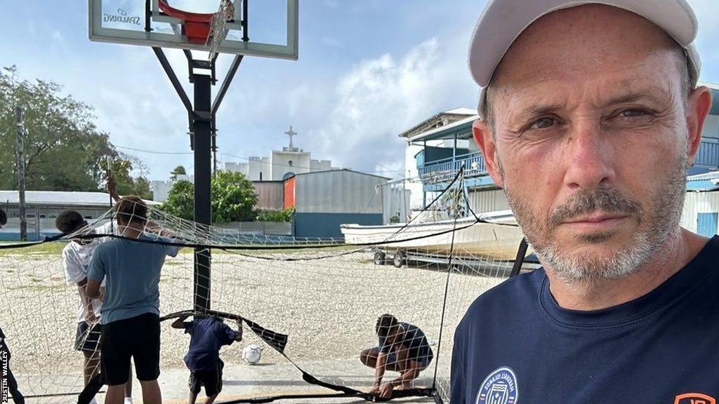 Justin Walley stands on a basketball court as young players set up a football goal