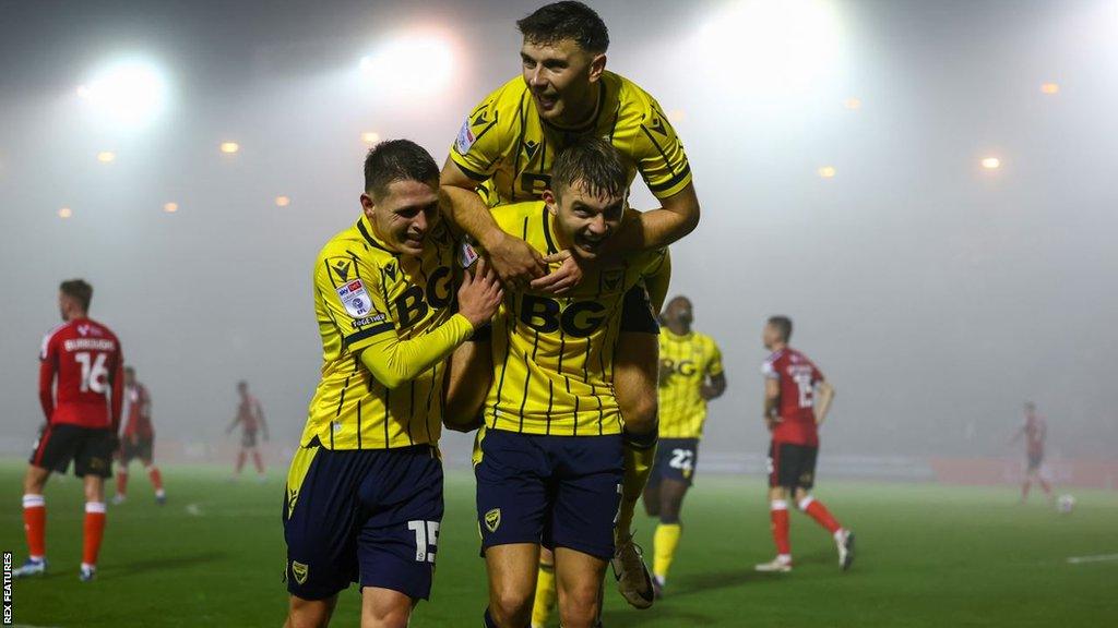 Oxford United celebrate their second goal against Lincoln on a misty and foggy night.