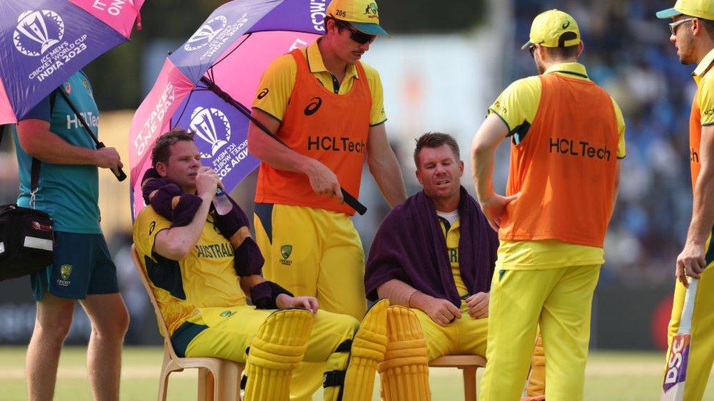 Australia batters Steve Smith and David Warner rest on plastic seats under umbrellas during a break for drinks