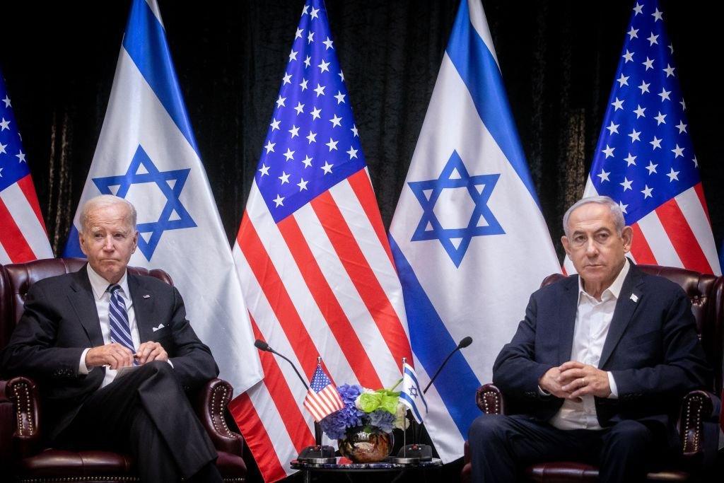 US President Joe Biden sits with Israeli Prime Minister Benjamin Netanyahu at the start of the Israeli war cabinet meeting in Tel Aviv on 18 October against a backdrop of Israeli and American flags