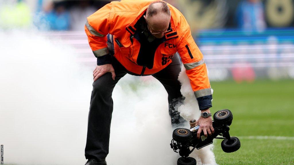 A steward picking up one of the remote control cars with a white smoke bomb attached