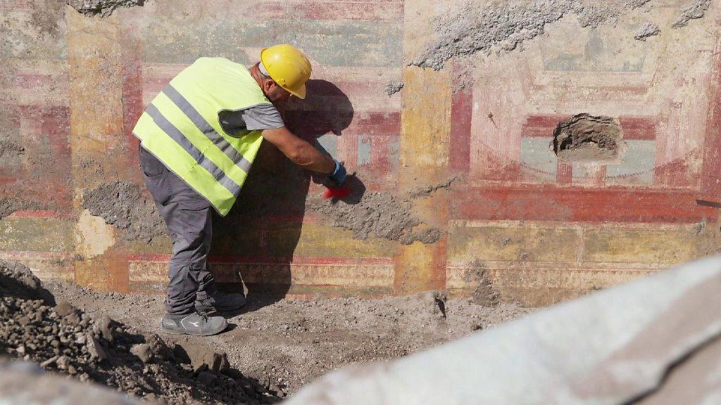 A person in a hi-vis jacket clears debris from a wall painting.