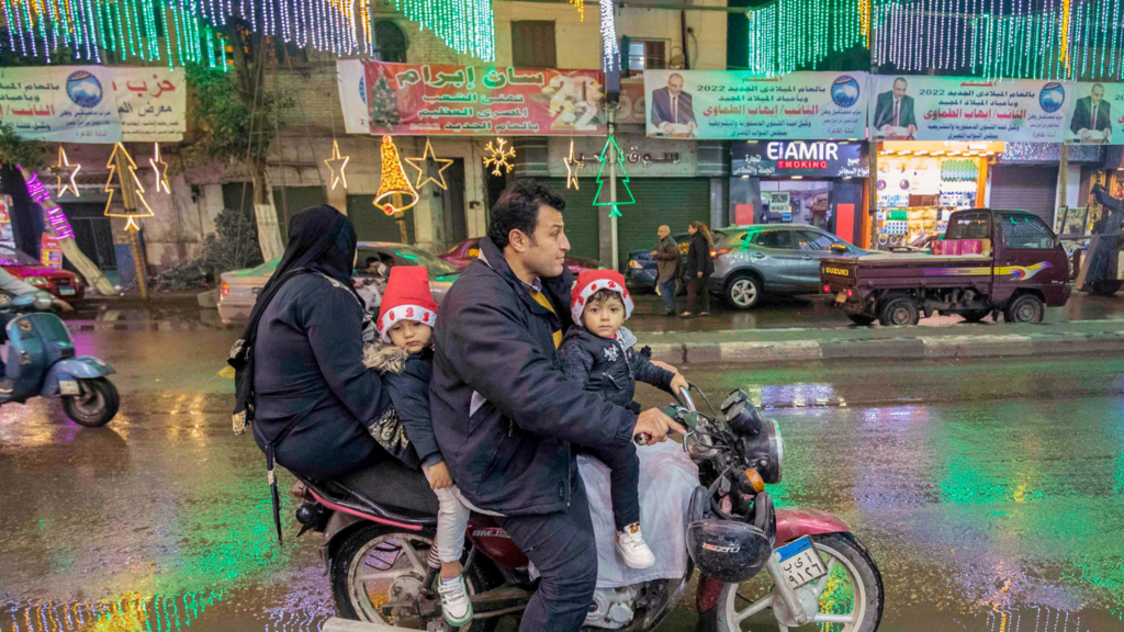 A man rides a scooter with a woman and children along a main street adorned with decorations in a suburb of the Egyptian capital, Cairo which is home to a large Christian population that celebrates Christmas Day on 7 January