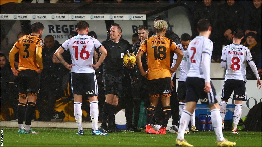 Players from both teams are taken off the pitch by the referee