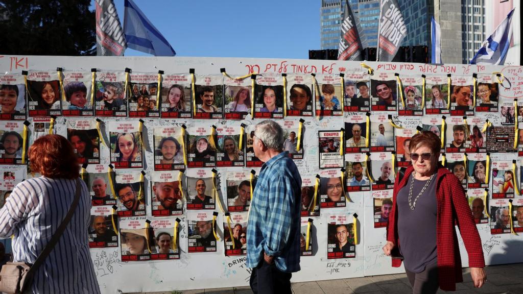 People walk past a wall with posters depicting missing people, on the day of a a demonstration called by mothers of hostages kidnapped on the deadly October 7 attack by Palestinian Islamist group Hamas, amid a temporary truce, in Tel Aviv, Israel, November 30, 2023.