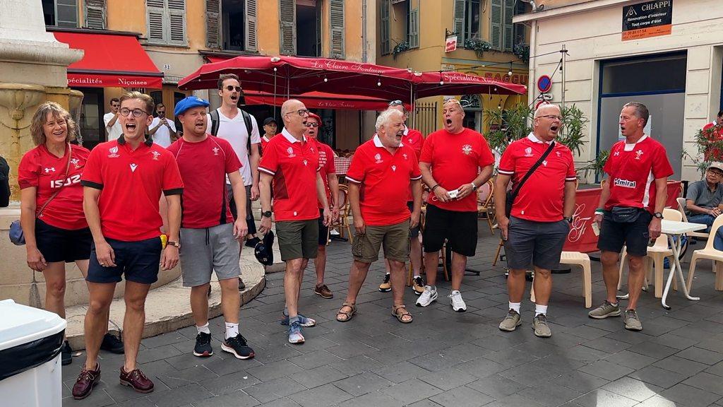 a group of menand women in red shirts singing in front of the street seating at a restaurant in Nice