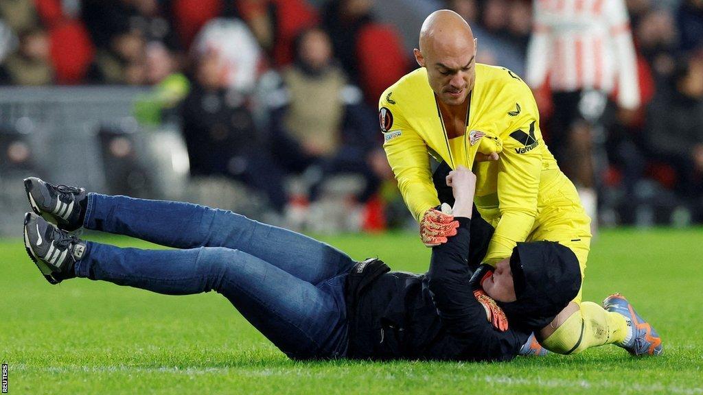 A pitch invader clashes with Sevilla goalkeeper Marko Dmitrovic