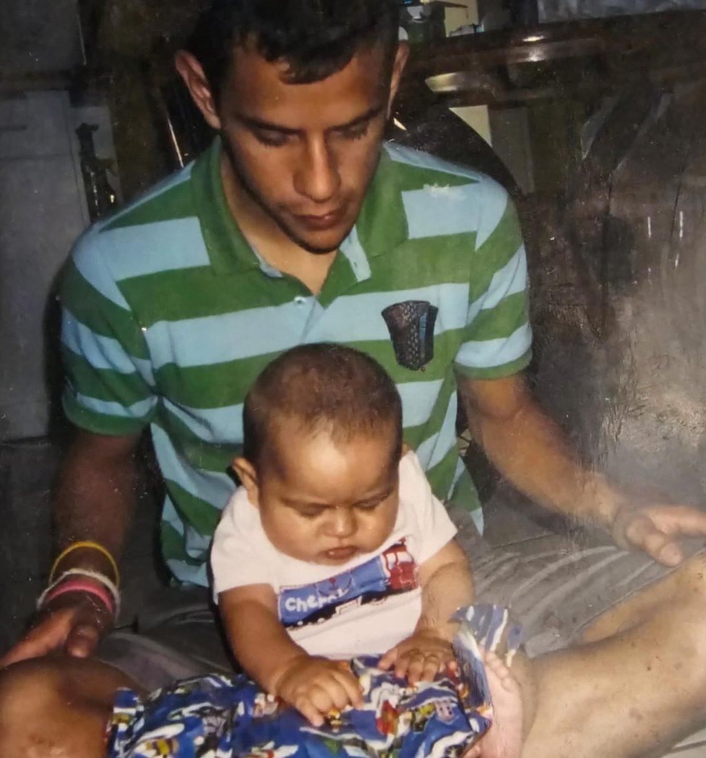 Felipe Nystrom sits with his infant son, who is unwrapping a present