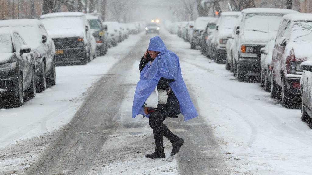 A person crosses the street as snow falls in the Brooklyn borough of New York City on February 13, 2024