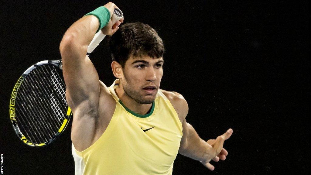 Carlos Alcaraz hits a forehand shot wearing a yellow Nike vest and a green sweatband