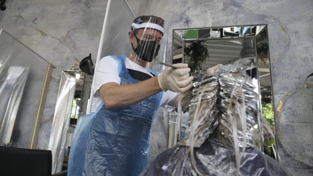 Hairdresser cuts hair wearing PPE