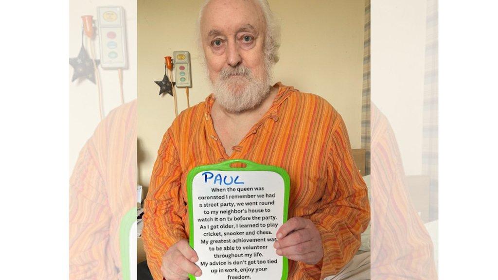 Paul wearing an orange top and holing up his message to share.