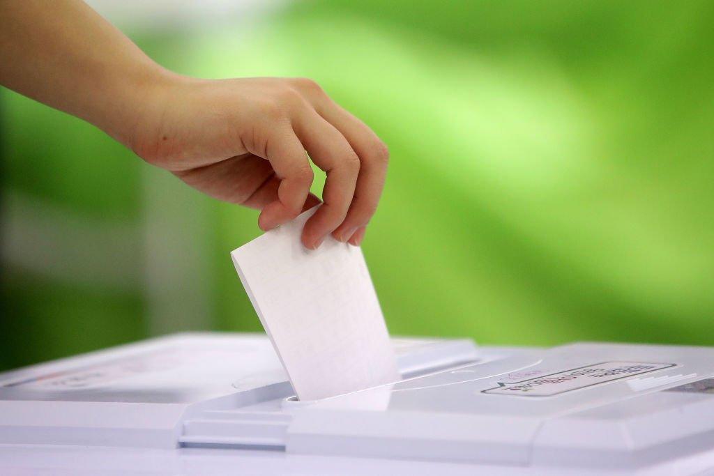 A person puts their voting paper in a ballot box