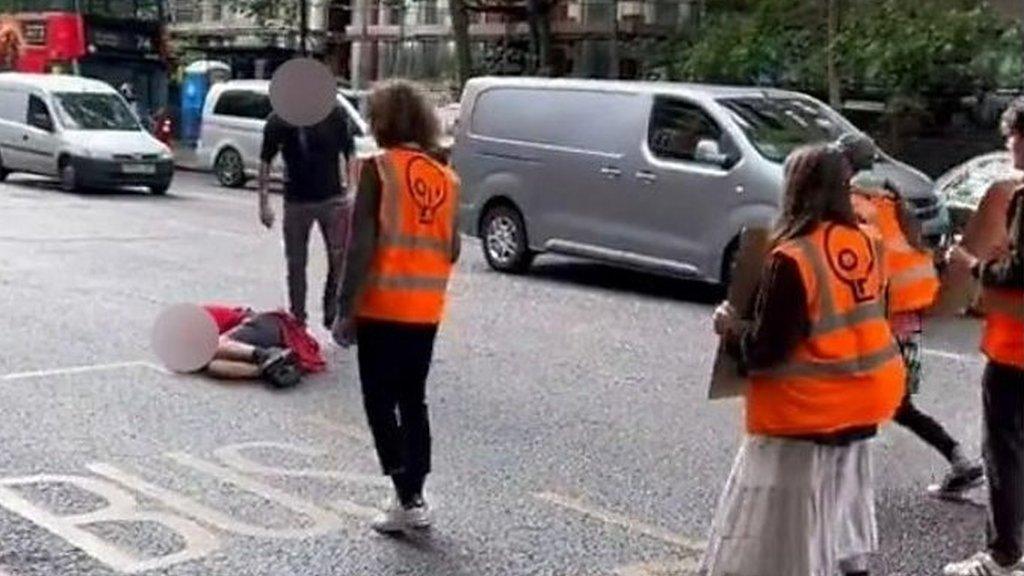 A protester lies on the ground while a man stands over him.