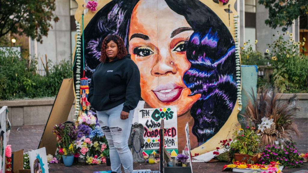 Breonna Taylor's mother stands in front of a mural with her image