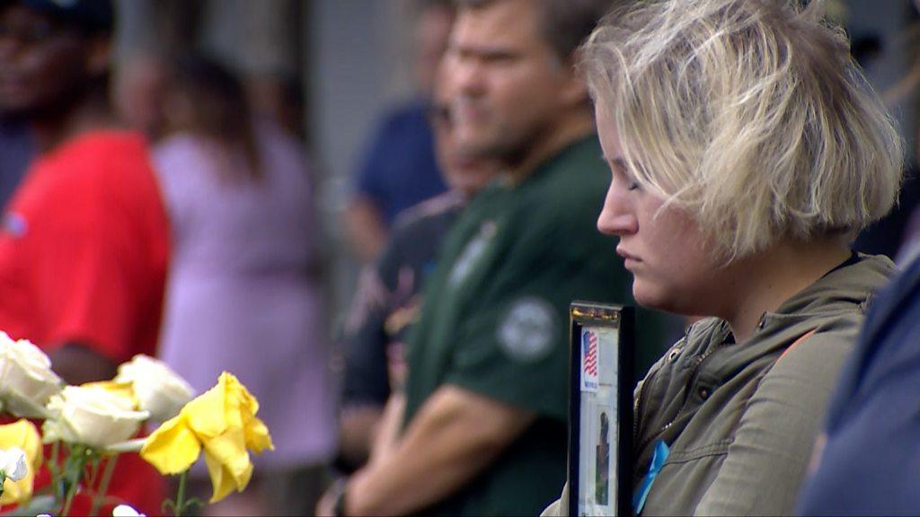 Woman holding photo frame stands in front of 9/11 memorial