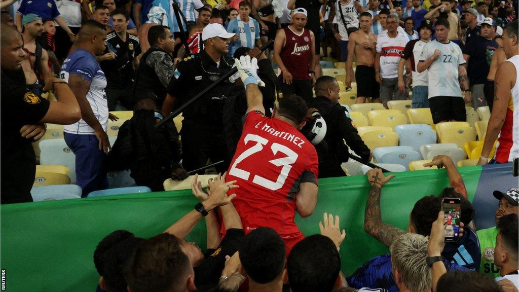 Argentina goalkeeper Emi Martinez trying to grab a baton out of a police officer's hand