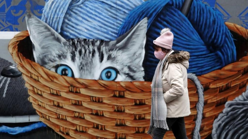 A woman in a mask walks past a mural in Glasgow