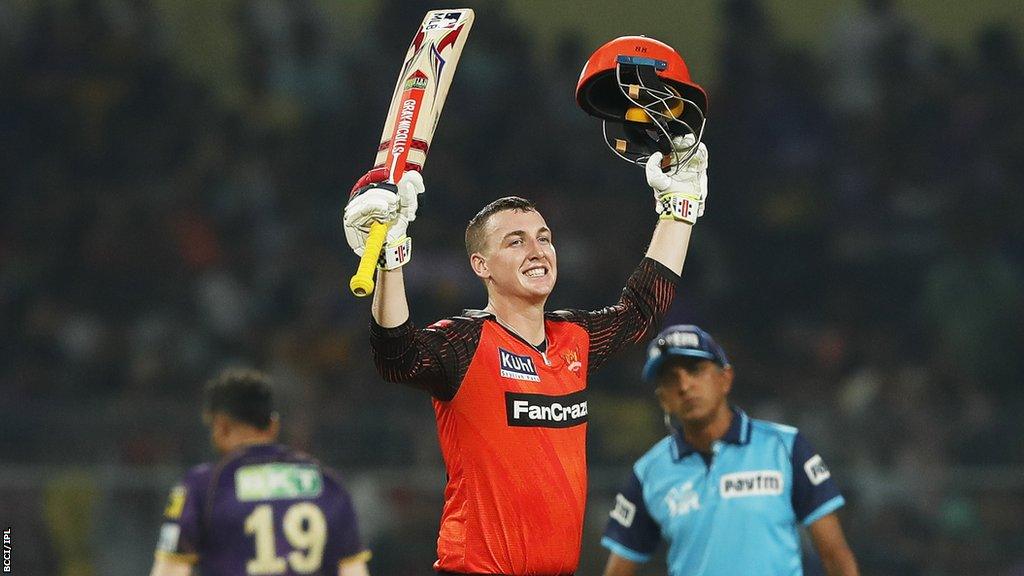 Sunrisers Hyderabad batter Harry Brook smiles as he raises his bat and helmet in celebration after hitting his first Indian Premier League century