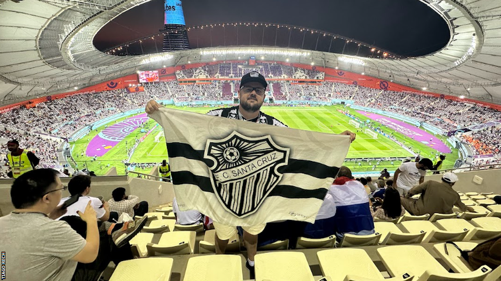 Tiago Rech holds aloft an FC Santa Cruz flag at the World Cup in Qatar in 2022