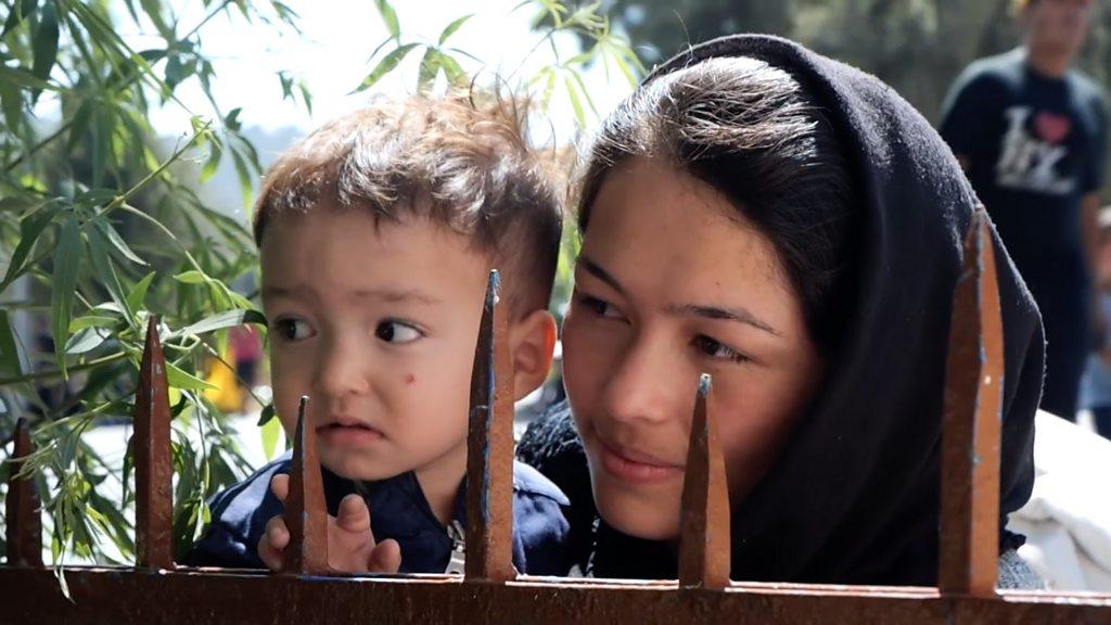 A woman and child look over a barrier at Moria camp