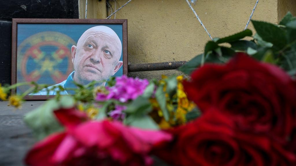 A framed image of Yevgeny Prigozhin is seen with floral tributes in the foreground