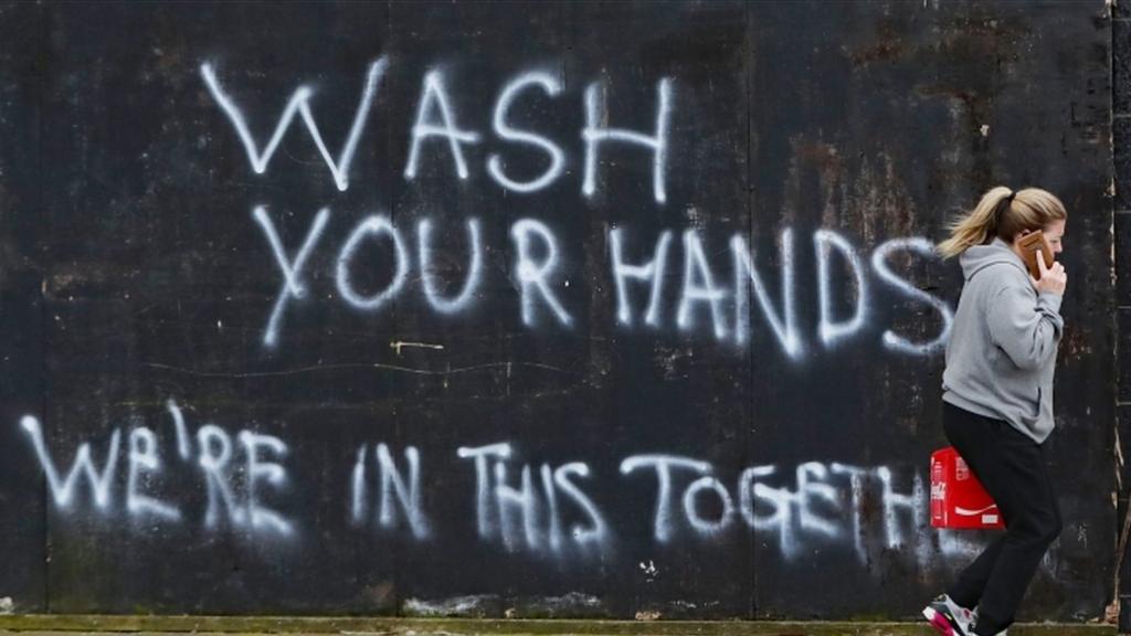 A woman walks past graffiti calling on people to wash their hands during the Covid-19