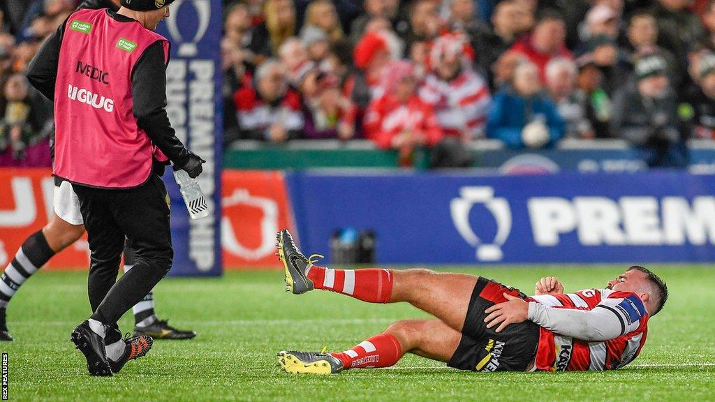 George McGuigan lies on the pitch injured as a medic comes on to help him