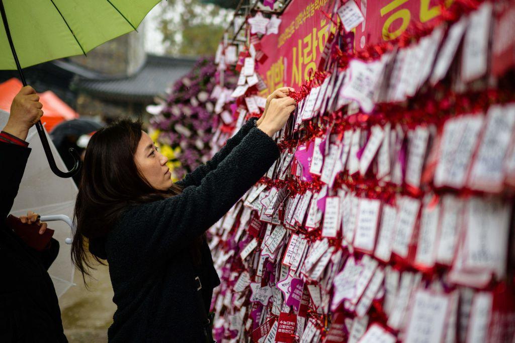 A woman places a handwritten note on a board at the Jogyesa Buddhist temple