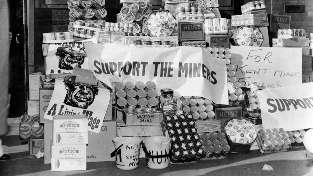 Lots of food is piled together with banners drapped over it, reading support for miners. 