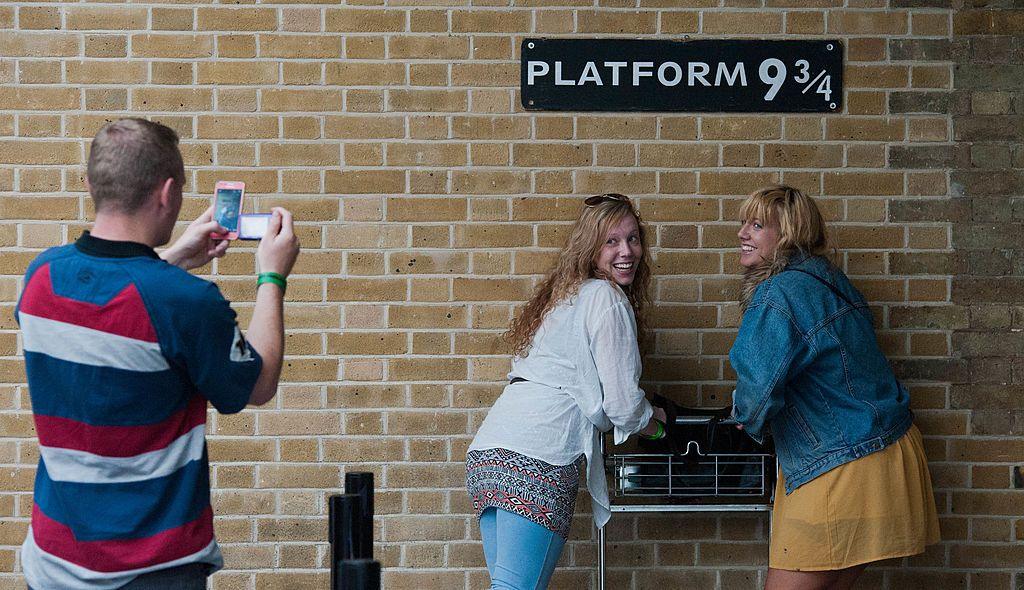 Tourists pose for photographs in front of the sign for Platform 9 3/4, the fictional platform in the Harry Potter Books at Kings Cross Station in London