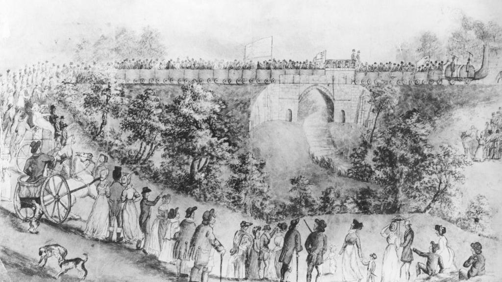A black and white sketch showing a crowd of people in tall hats and long dresses watching as a train of wagons pulled by a steam engine crosses a stone bridge