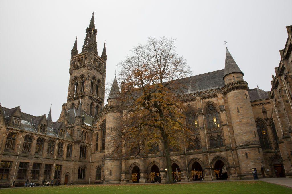 Glasgow University's main building, pictured from the courtyard look towards the turrets and windows on one side of the gothic building. A tree is shedding orange leaves on the grass
