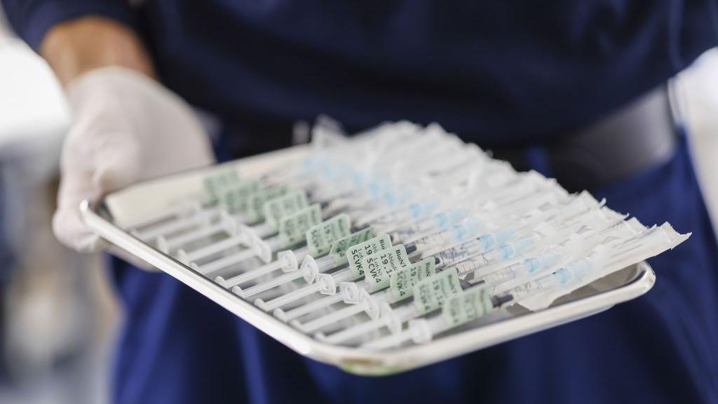 A hand in a latex glove holds a tray of syringes filled with the Pfizer-BioNTech vaccine for Covid-19 at a vaccination centre in Munich, Germany, on Thursday, 2 Dec 2021