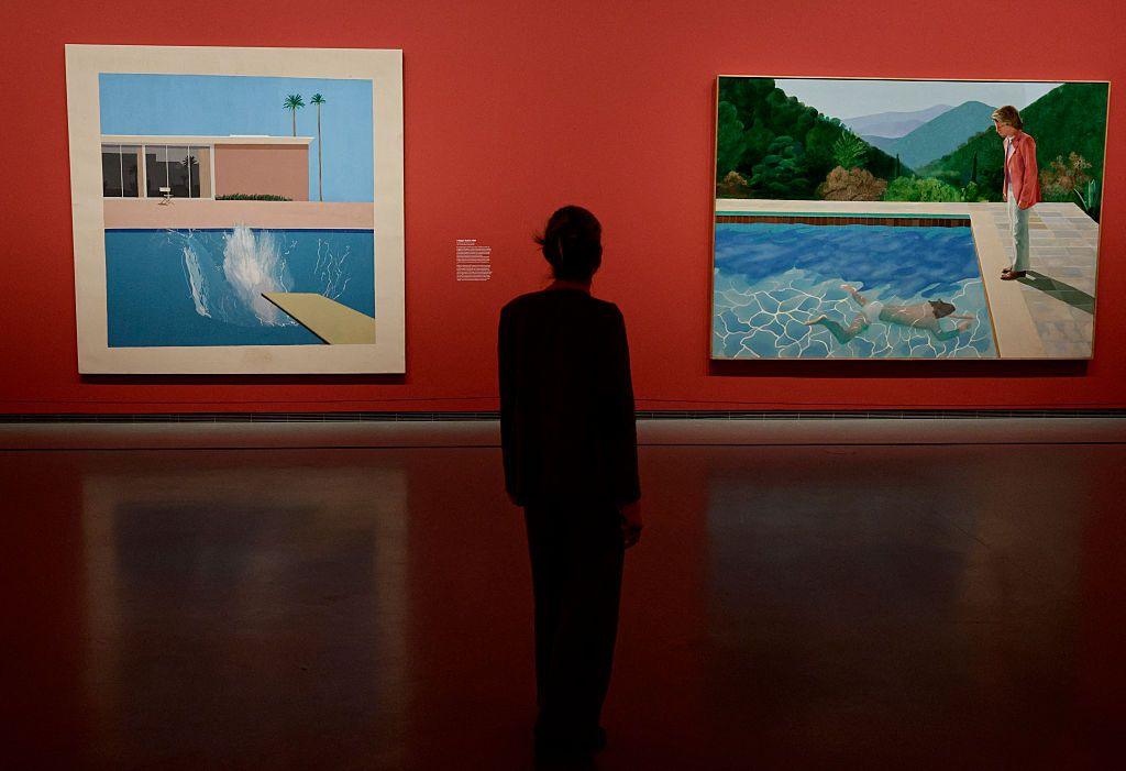 Shadowy figure stands in front of the two paintings displayed on a red wall in an art gallery