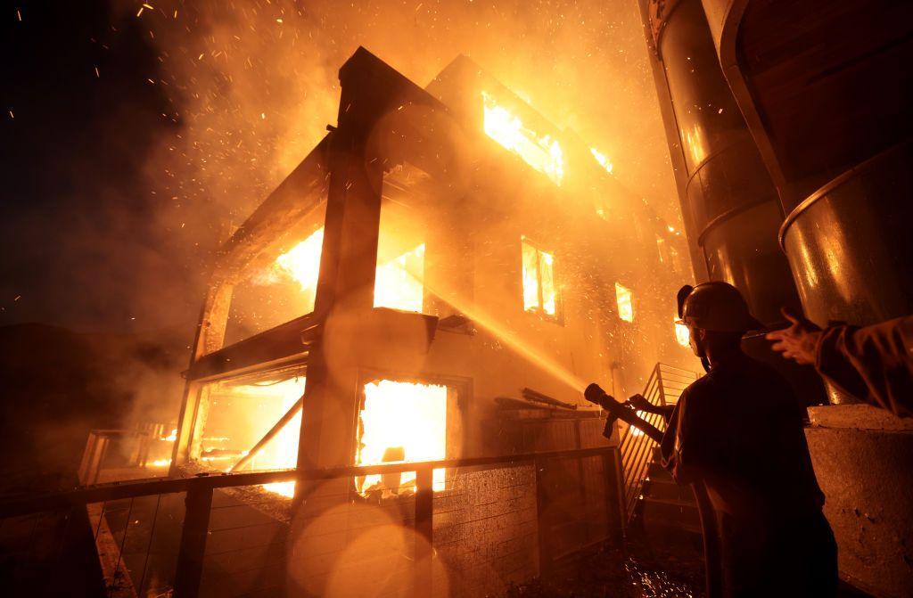 A night-time photo shows fire destroying a three-storey property as a firefighter in the bottom right of the images shoots water at the building.