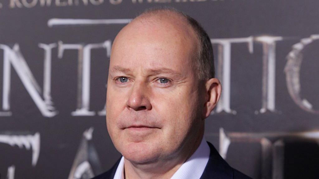 balding man in front of film poster