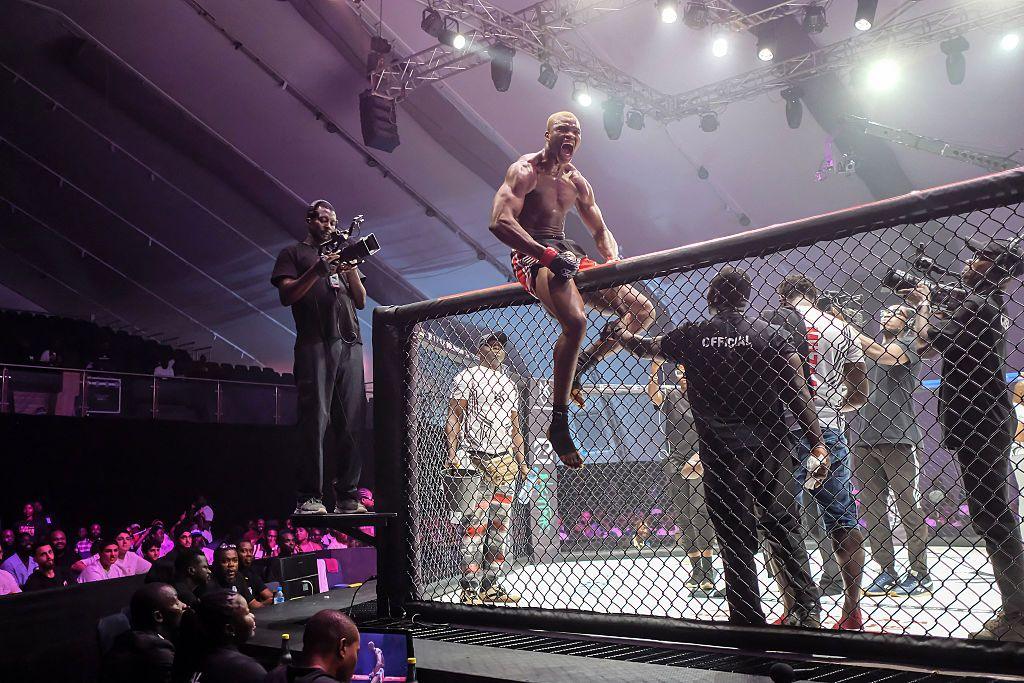 Nigerian professional MMA fighter Richard Muzaan climbs the fight cage and shouts to fans after winning.