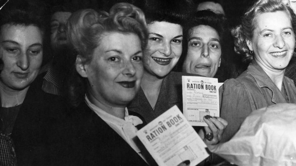 Black-and-white photograph of women in the 1940s holding up their ration books.  