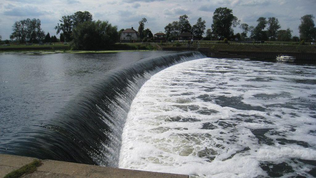 An image of Cromwell Weir on a sunny day. You can see the water bubbling and foaming at the bottom of it.