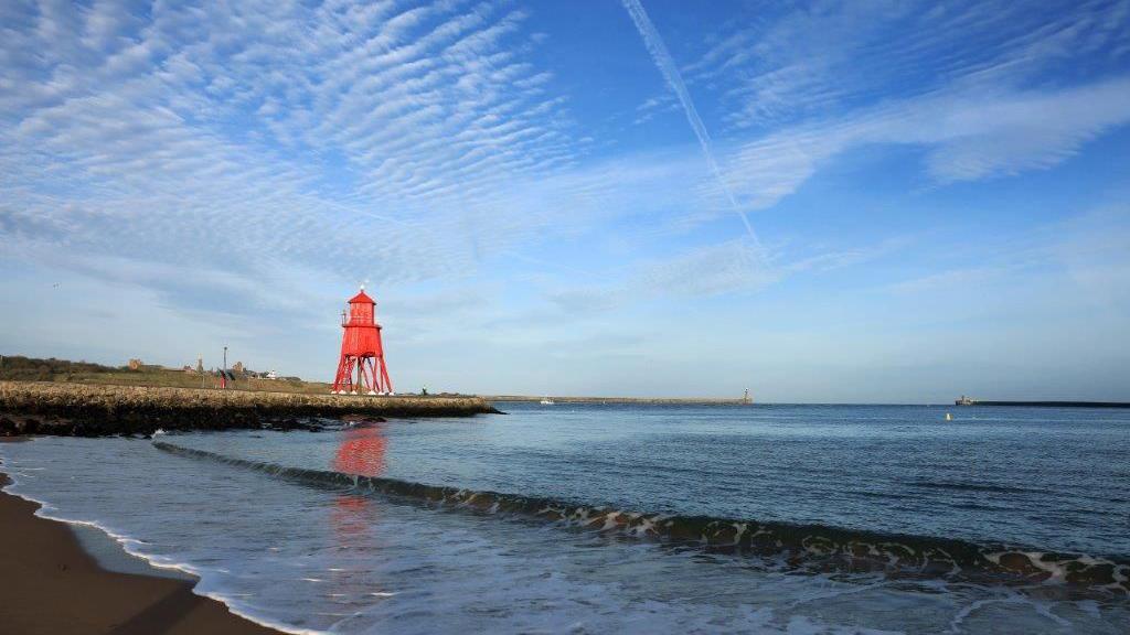 Herd Groyne lighthouse, pictured on the left, looking out over the mouth of the River Tyne towards the North Sea on a sunny day.