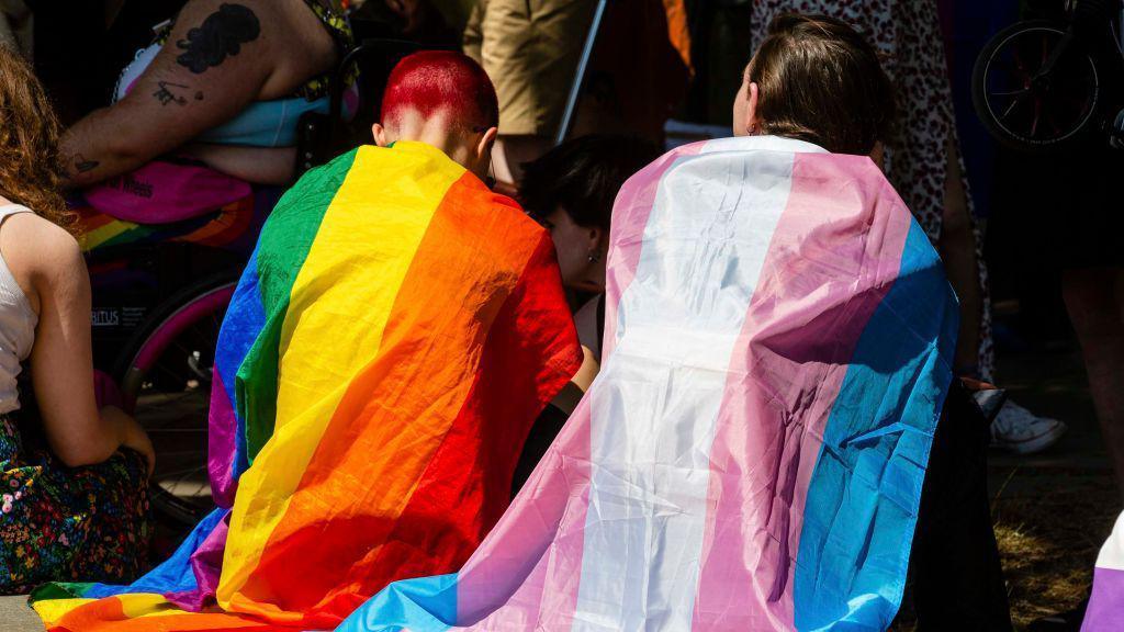 People draped in Rainbow Pride and transgender flags sit in London in 2022