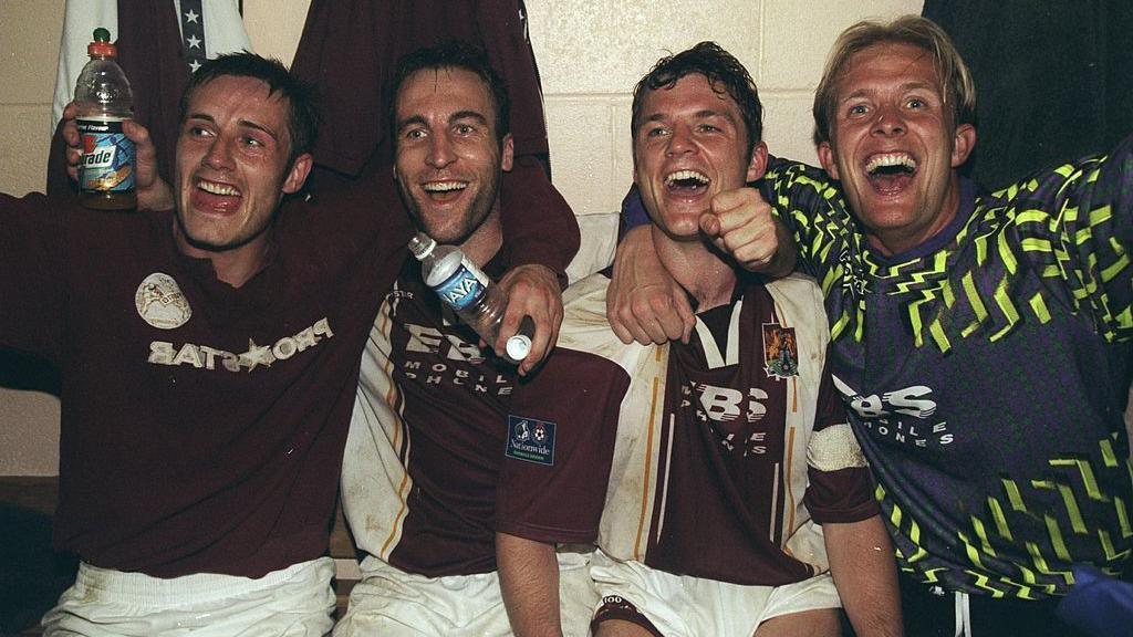 Four Northampton Town players celebrating in the dressing room of Sixfields