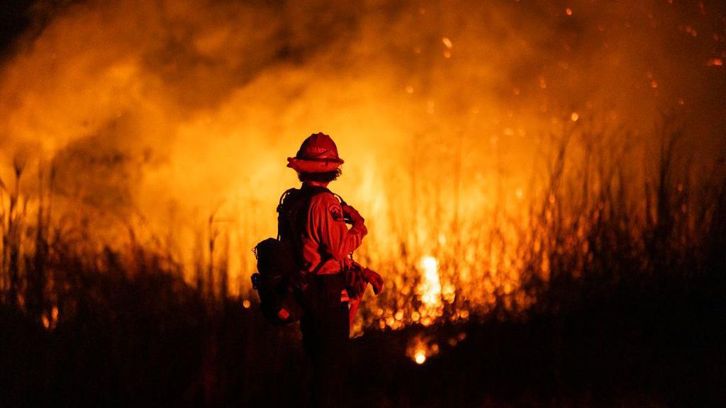 A firefighter stands in silhouette against wildfires