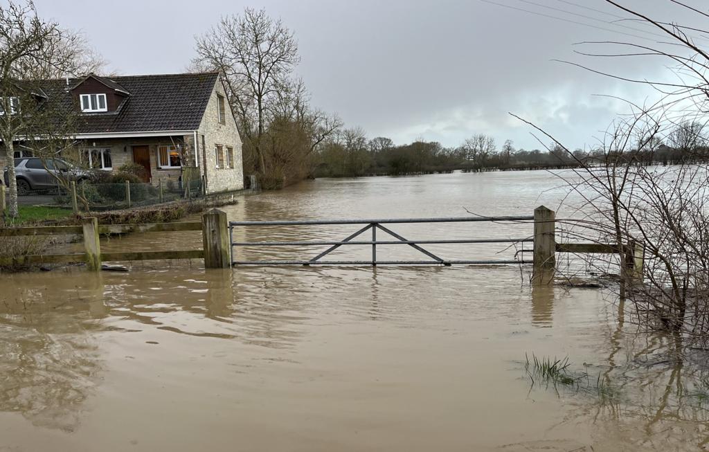 A house is visible surrounded by flood water in Somerset with a partly submerged gate in front of it