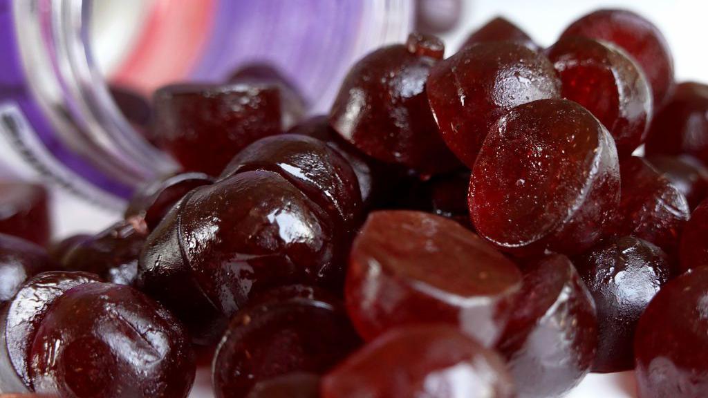 A collection of burgundy-coloured melatonin chews are poured from a jar.